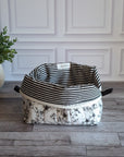 A fabric quilted toiletry with a black and white striped lining and a black-and-white floral patterned outer, placed on a gray wood floor in front of a white paneled wall.
