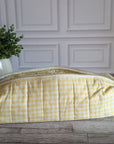 A yellow and white gingham quilted cosmetic bag with a floral patterned interior lining, resting on a gray wooden floor in front of a white paneled wall.