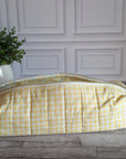 A yellow and white gingham quilted cosmetic bag with a floral patterned interior lining, resting on a gray wooden floor in front of a white paneled wall.