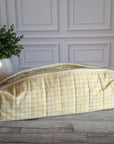 A yellow and white gingham quilted cosmetic bag with a floral patterned lining, resting on a gray wooden floor in front of a white paneled wall.