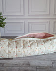 A quilted cylindrical cosmetic pouch with a cream and pink cherry pattern, shown open on a gray wood floor in front of a white paneled wall.