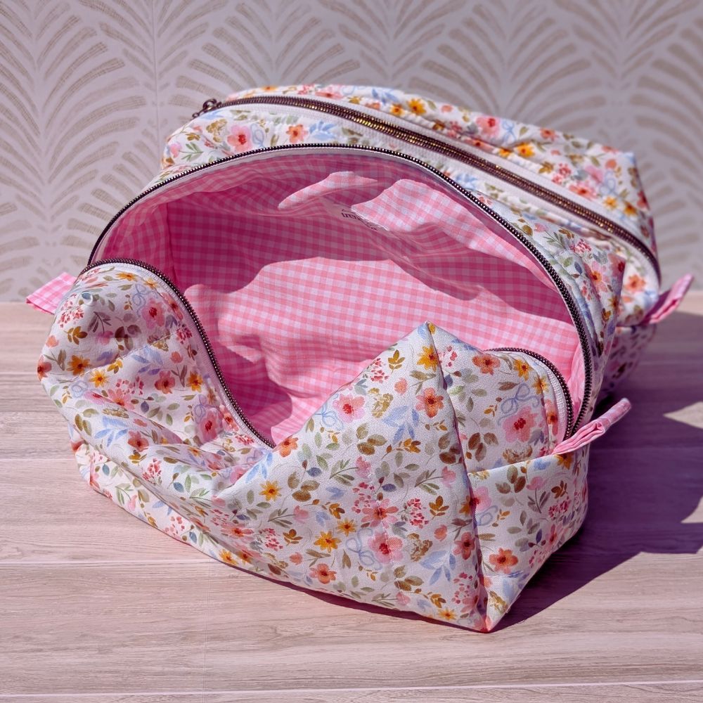 Floral-patterned toiletry bag with pink interior on a wooden surface