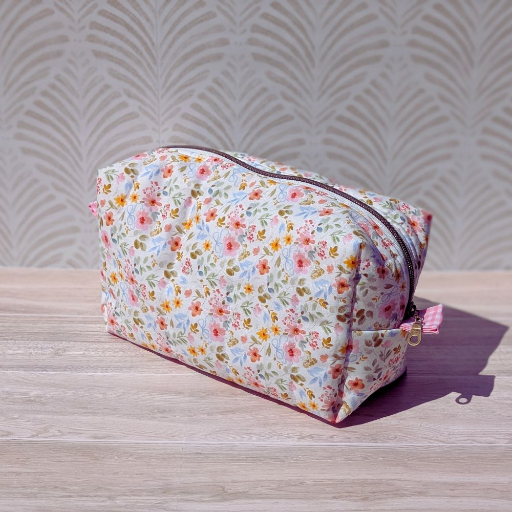 Floral-patterned toiletry bag on a wooden surface with a decorative wall background