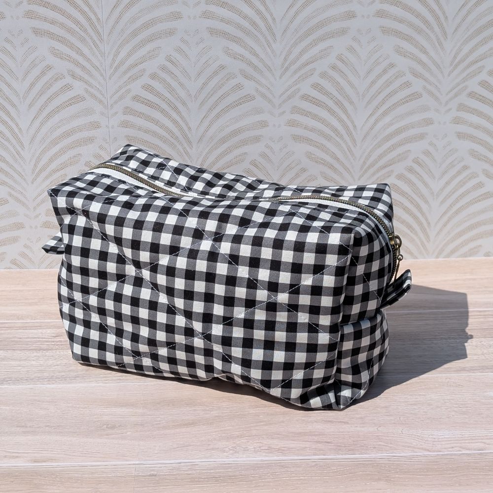 Black and white checkered toiletry bag on a wooden surface with a patterned wall in the background