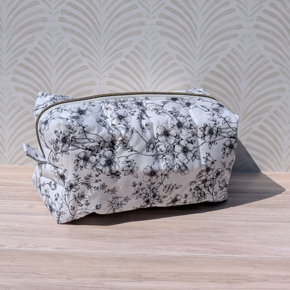 Floral-patterned makeup bag on a wooden surface with a decorative wall background
