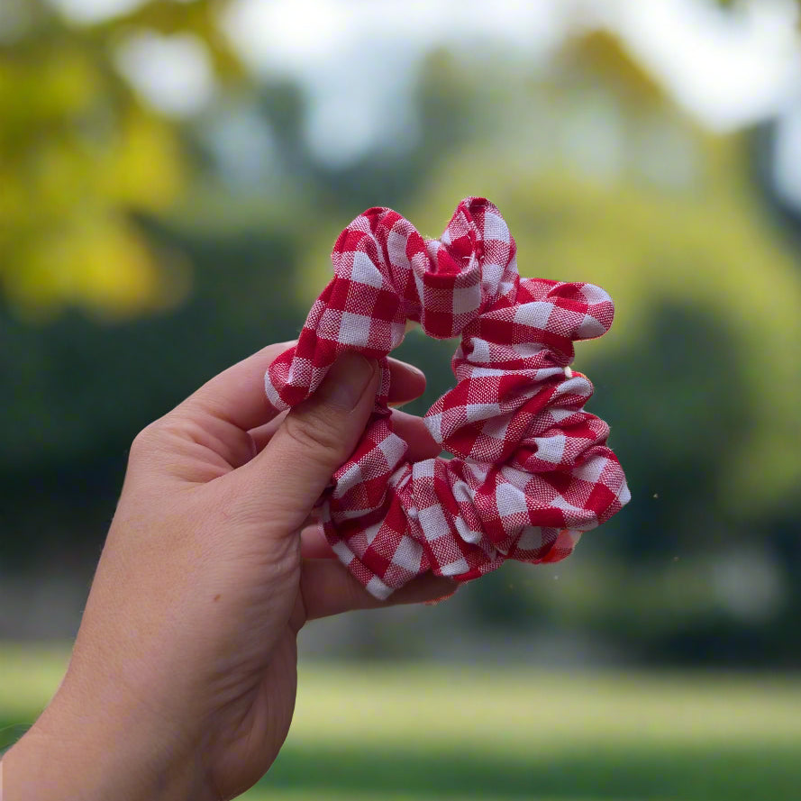 Red and white checkered scrunchie held in a hand with a suburban background