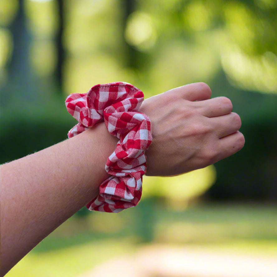 Red and white checkered scrunchie on a wrist with a blurred outdoor background
