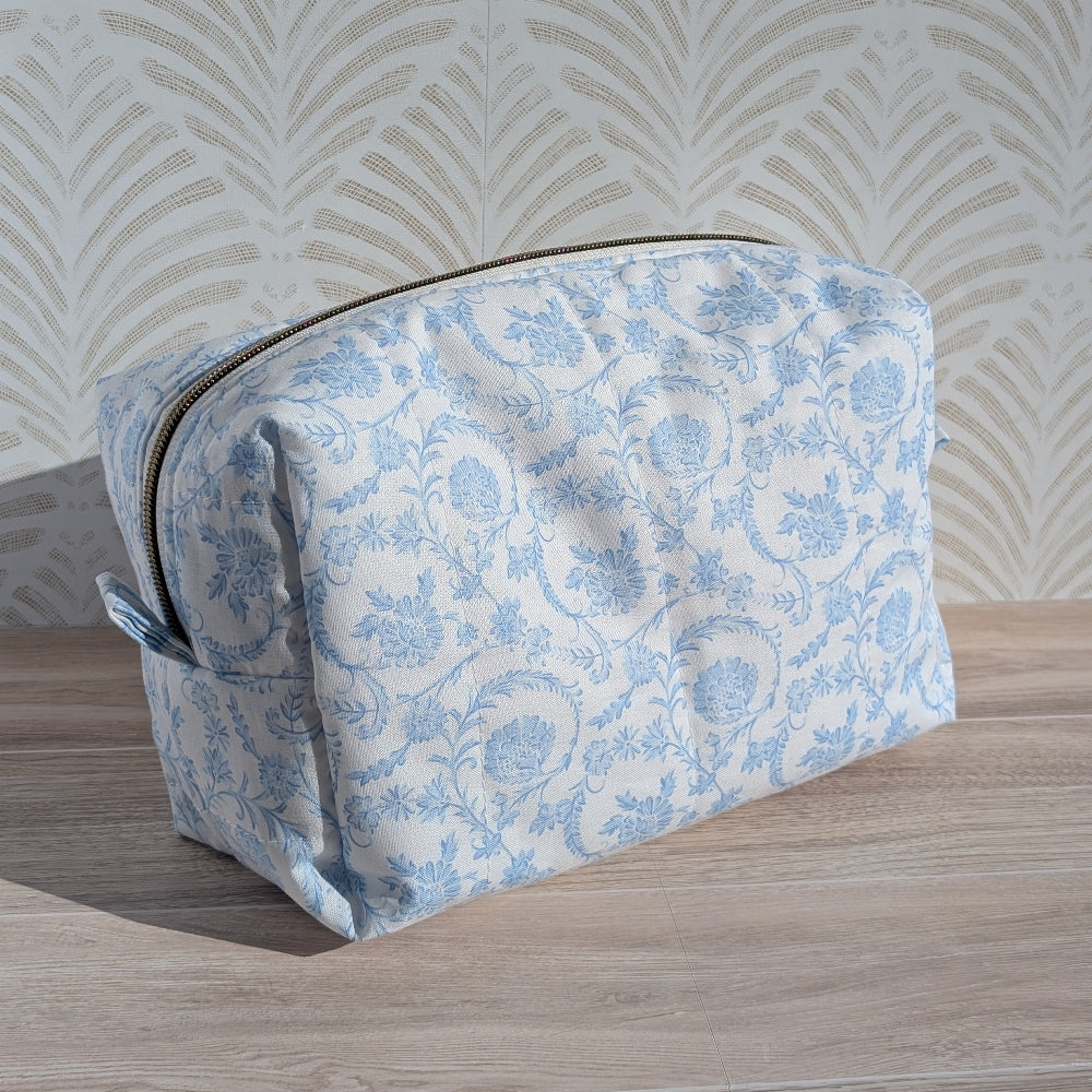 Blue floral-patterned pouch on a wooden surface with a decorative wall background