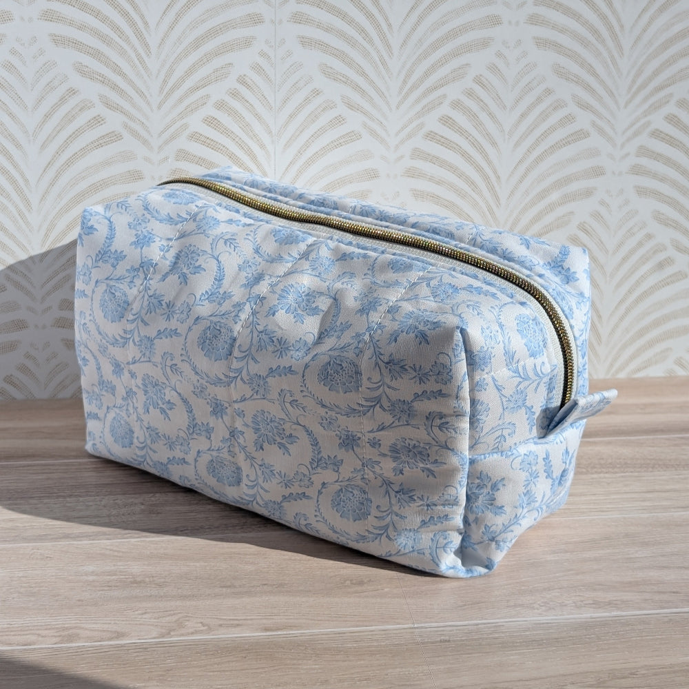Blue floral-patterned toiletry bag on a wooden surface with a light background