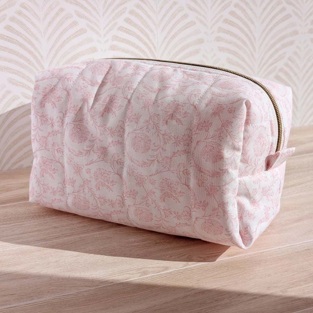 Pink floral-patterned toiletry bag on a wooden surface with a light background