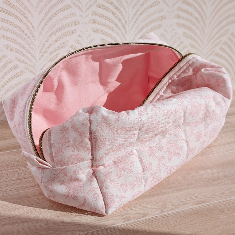 Floral-patterned makeup bag with pink interior on a wooden surface
