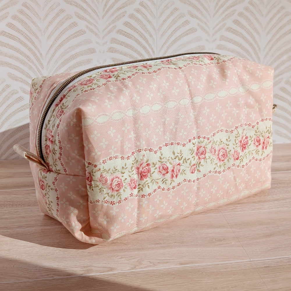 Pink floral toiletry bag on a wooden surface with a patterned wall in the background