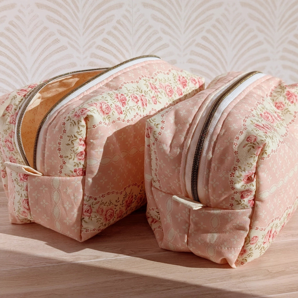Two floral-patterned toiletry bags on a wooden surface with a textured wall background.