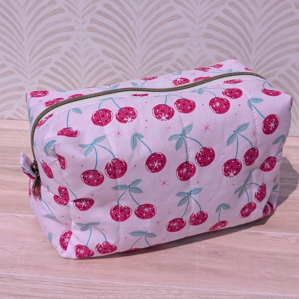 Cosmetic bag with cherry pattern on a wooden surface and light background