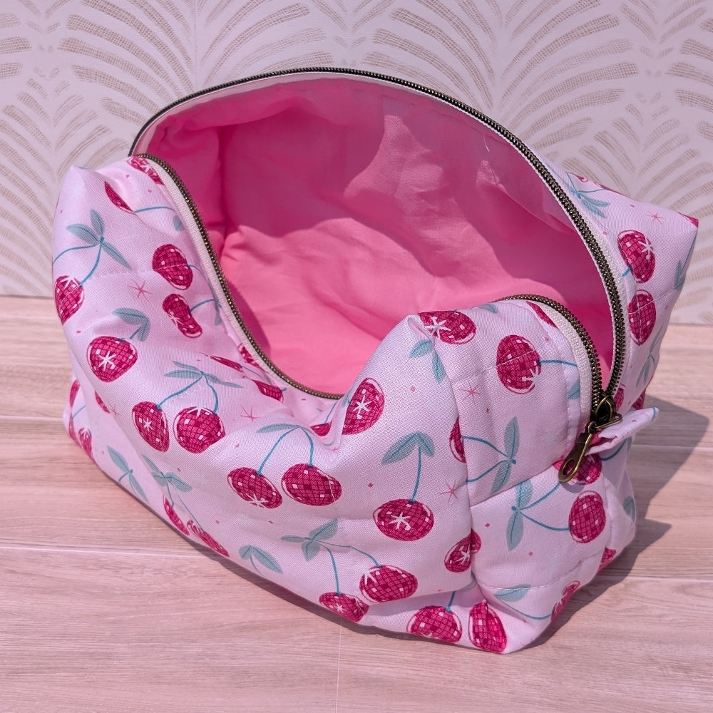 Pink fabric pouch with cherry pattern on a wooden surface