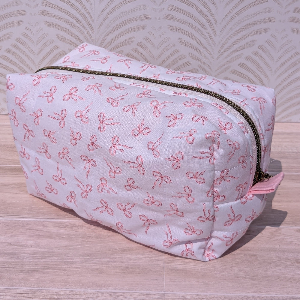 Pink toiletry bag with bow pattern on a wooden surface
