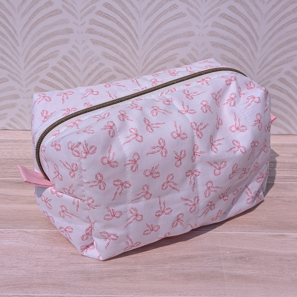 Pink toiletry bag with bow pattern on a wooden surface and patterned wall background
