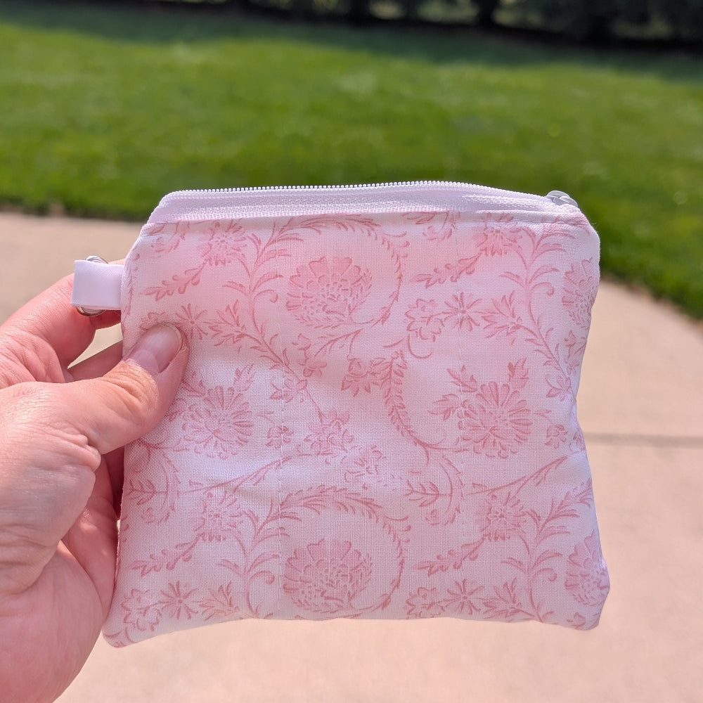 Pink floral-patterned pouch held by a hand with a blurred outdoor background