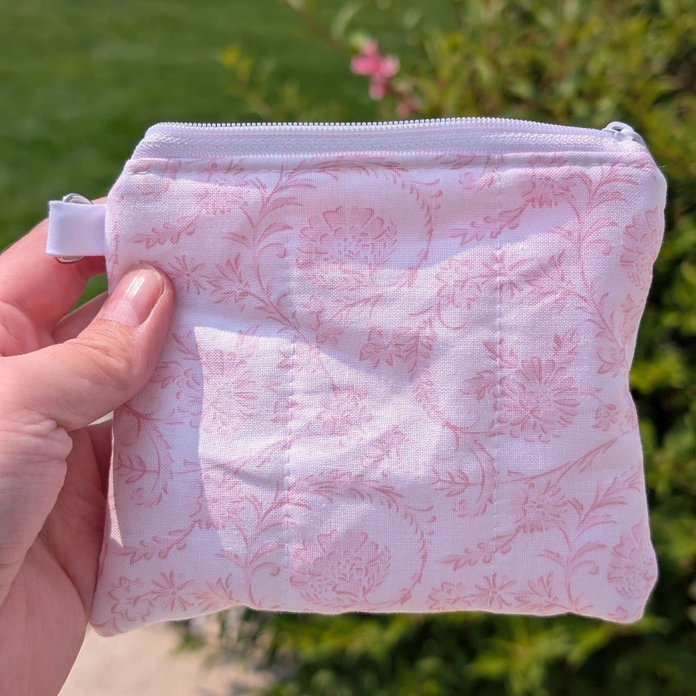 Pink floral-patterned pouch held by a hand with a blurred green outdoor background