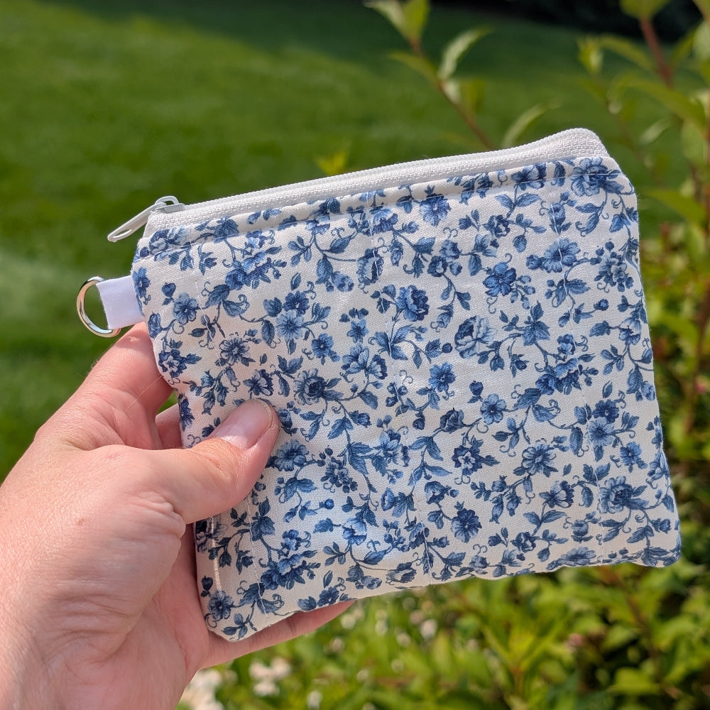 Hand holding a blue floral fabric pouch against a green outdoor background