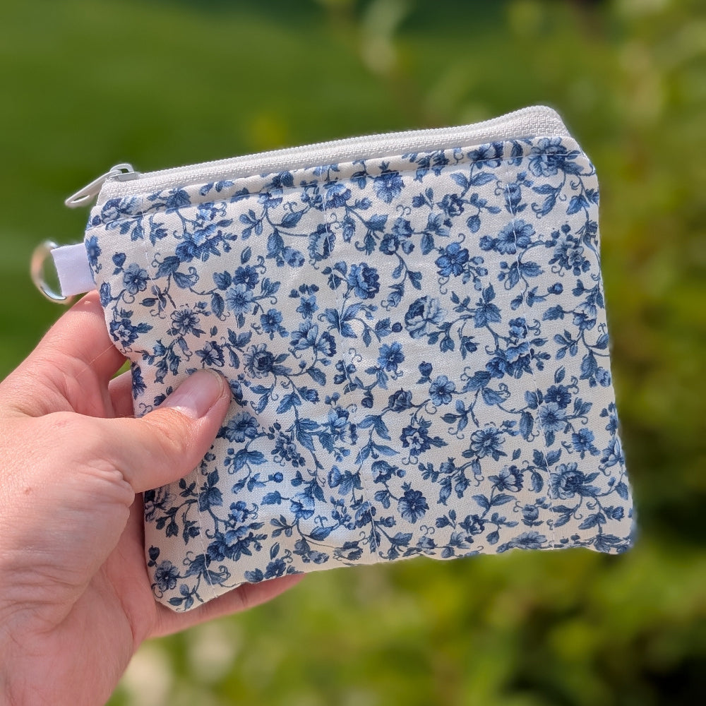 Hand holding a small blue floral-patterned pouch against a blurred green outdoor background