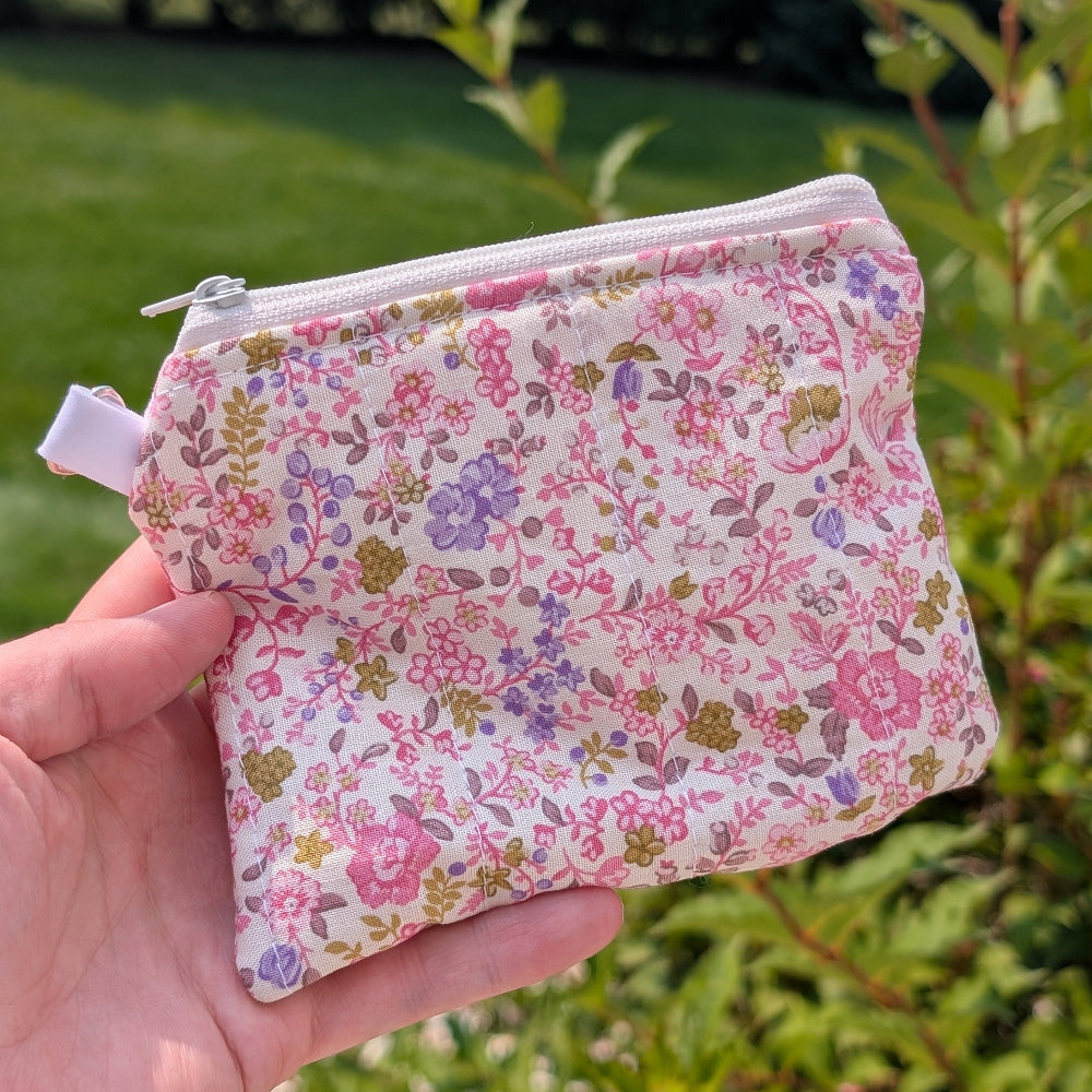 Floral-patterned pouch held in a hand with greenery in the background