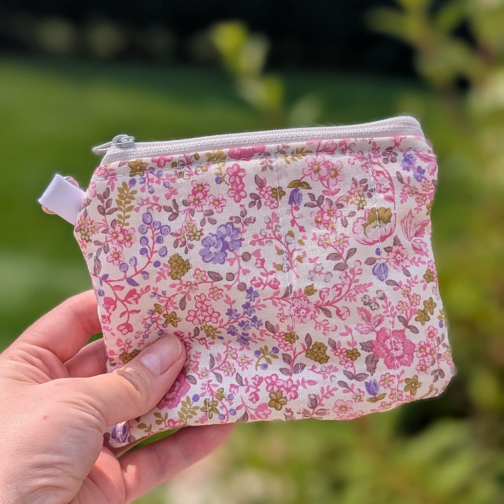 Hand holding a small floral-patterned pouch against a blurred green outdoor background
