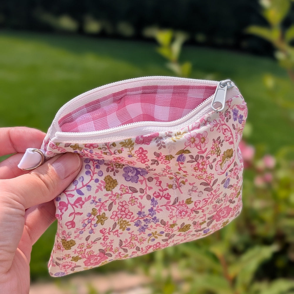 Hand holding a small floral fabric pouch with a pink interior against a blurred green outdoor background