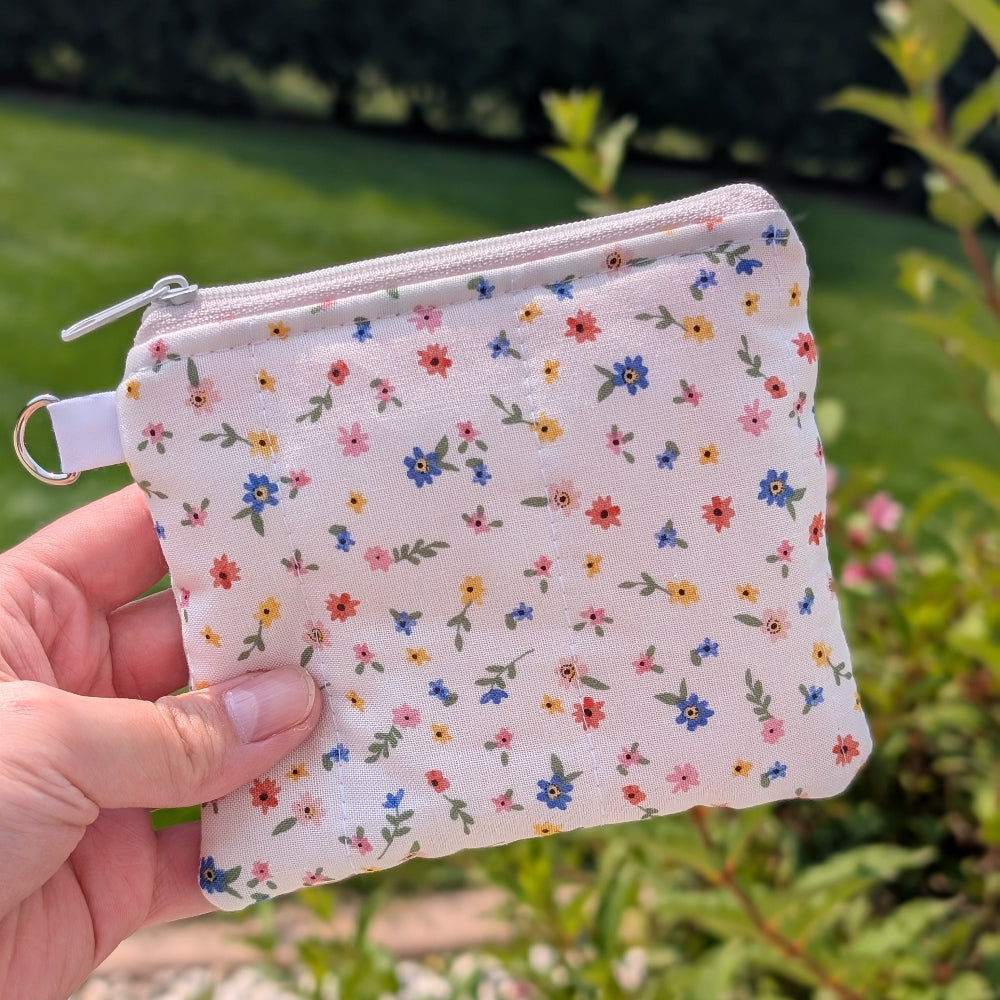 Small floral-patterned pouch held by a hand with a green outdoor background