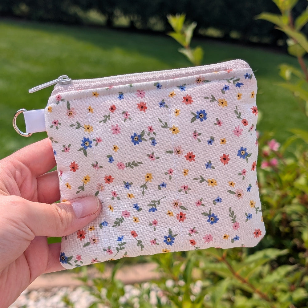 Small floral-patterned pouch held in a hand with a green outdoor background