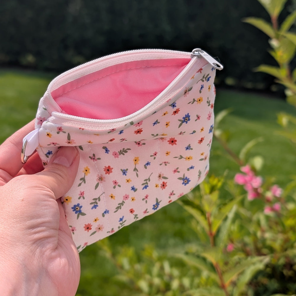 Hand holding a small floral-patterned pouch with a pink interior against a natural background.