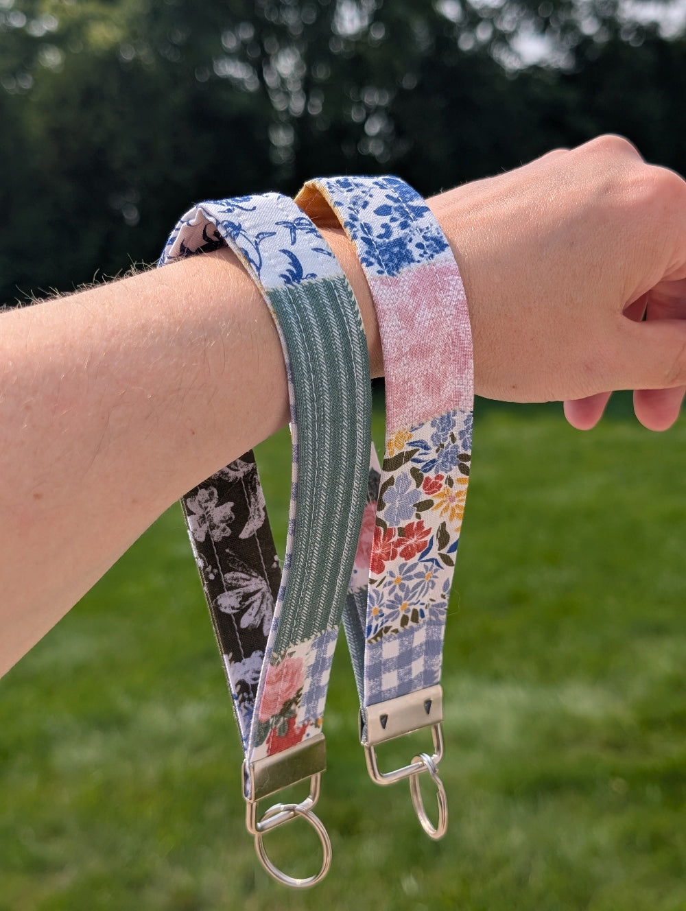 Hand wearing a floral patterned strap with a blurred green outdoor background