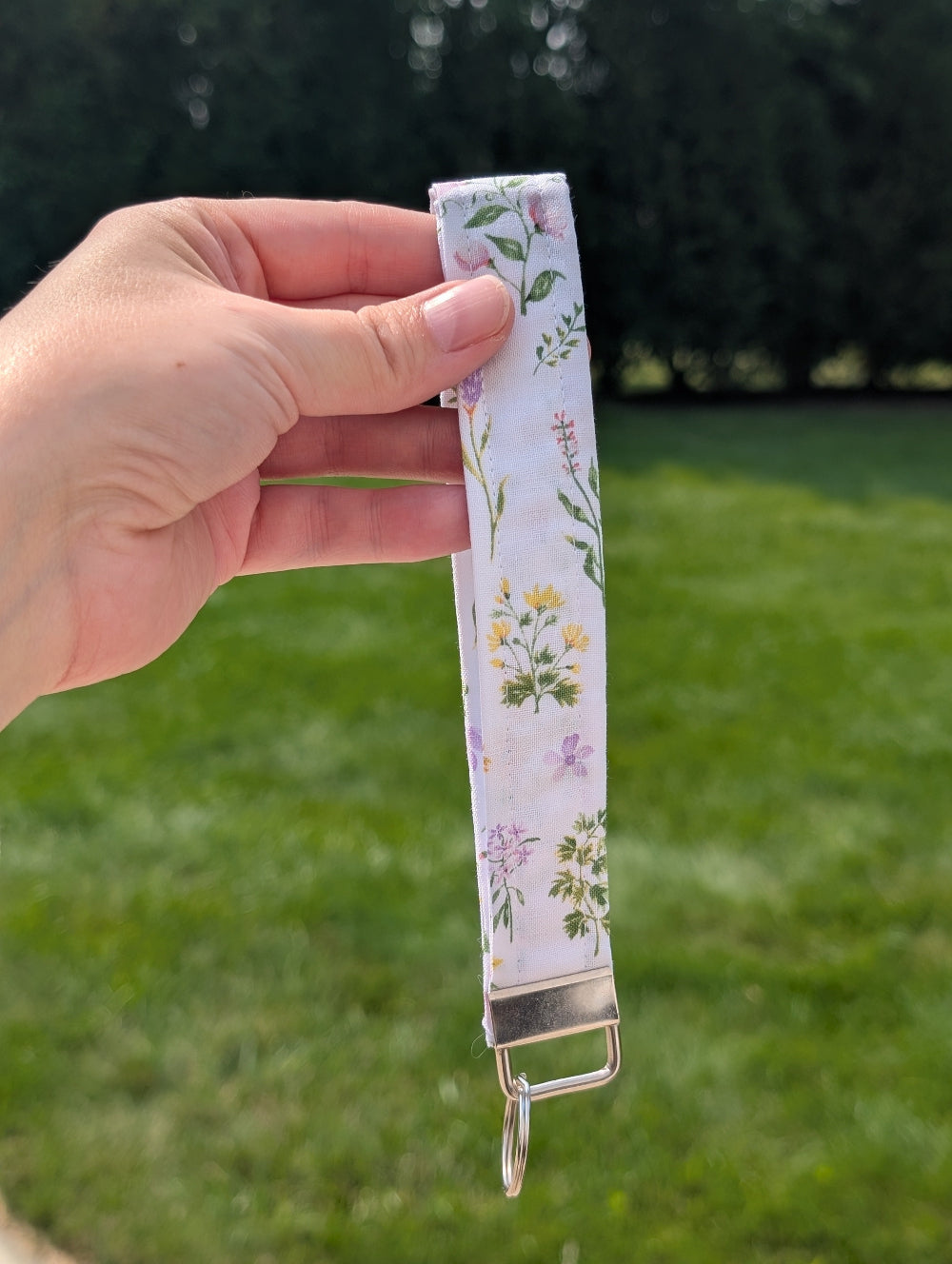 Hand holding a floral-patterned strap with a green grass background