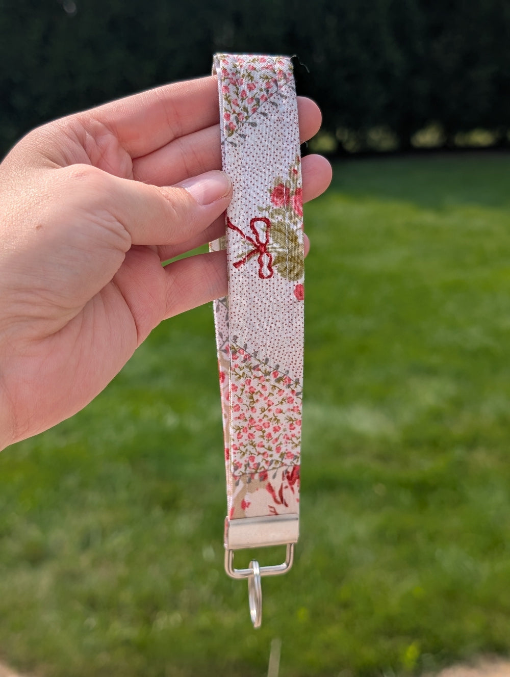 Fabric strap with floral design held by a hand against a grassy background