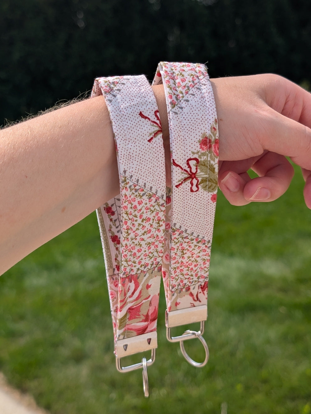 Floral patterned strap with keychain attachment held by a person against a blurred green background