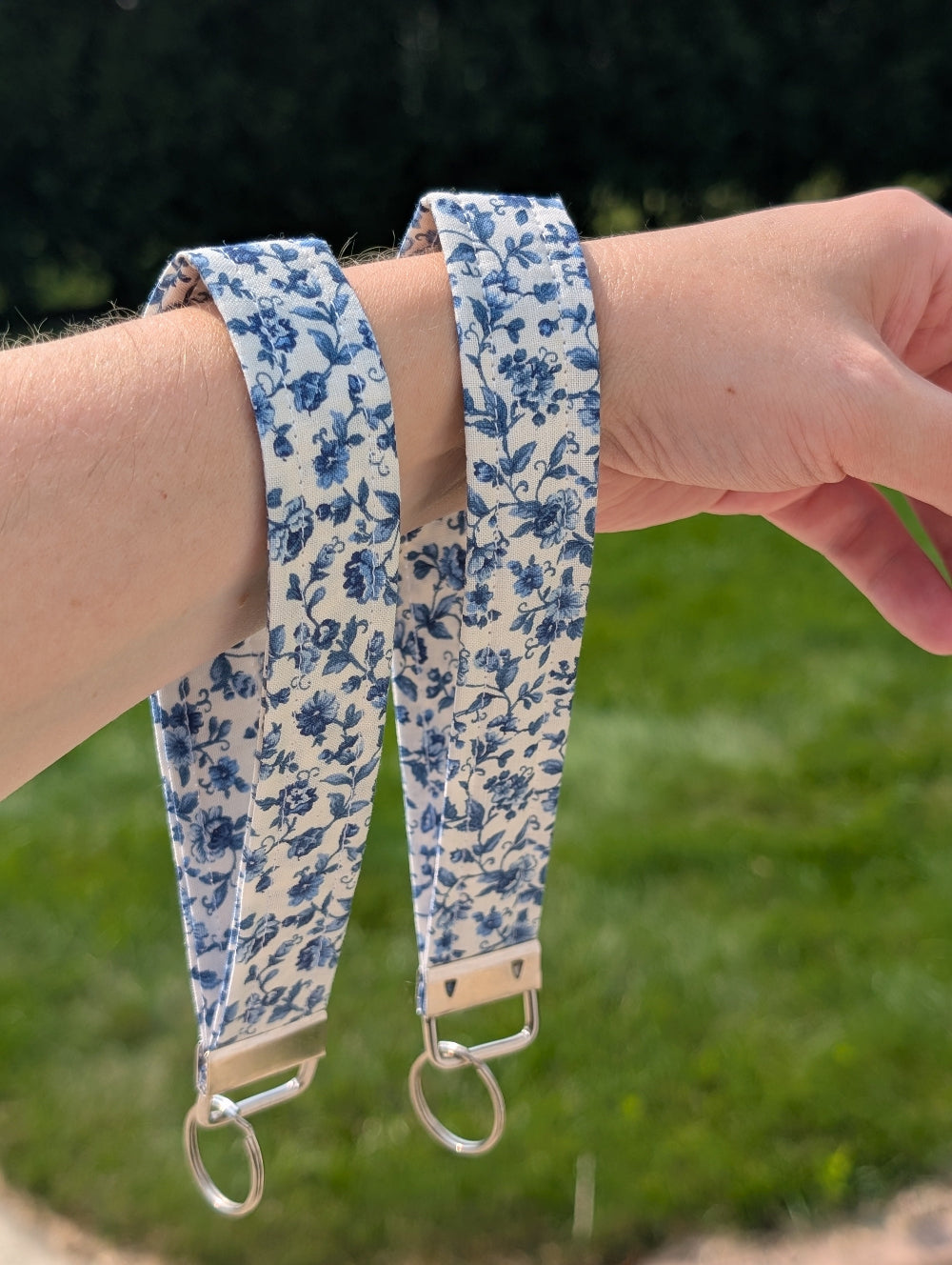 Blue floral strap held by a person against a grassy background
