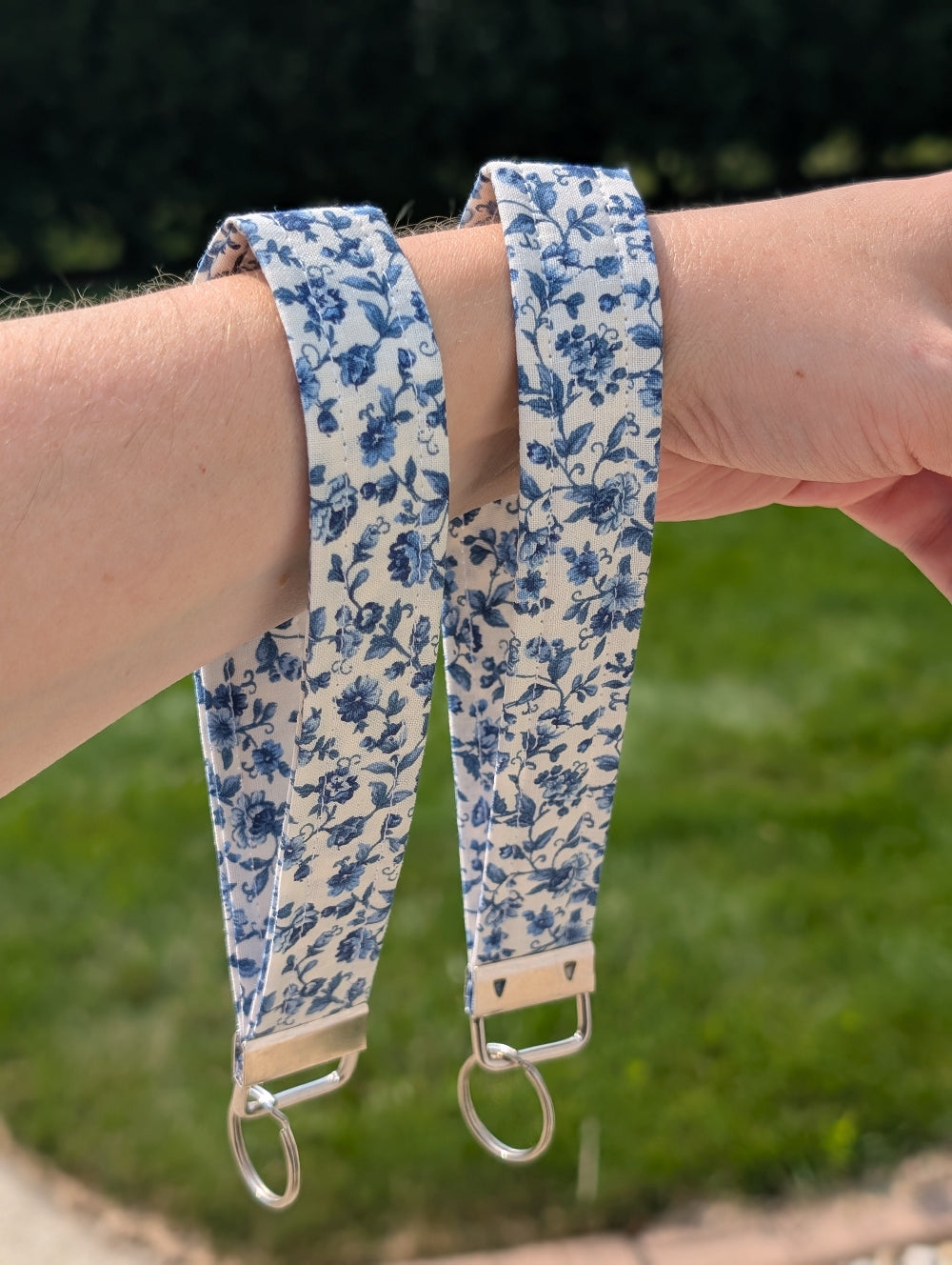 Floral-patterned strap with metal keychain held by a person against a blurred green background