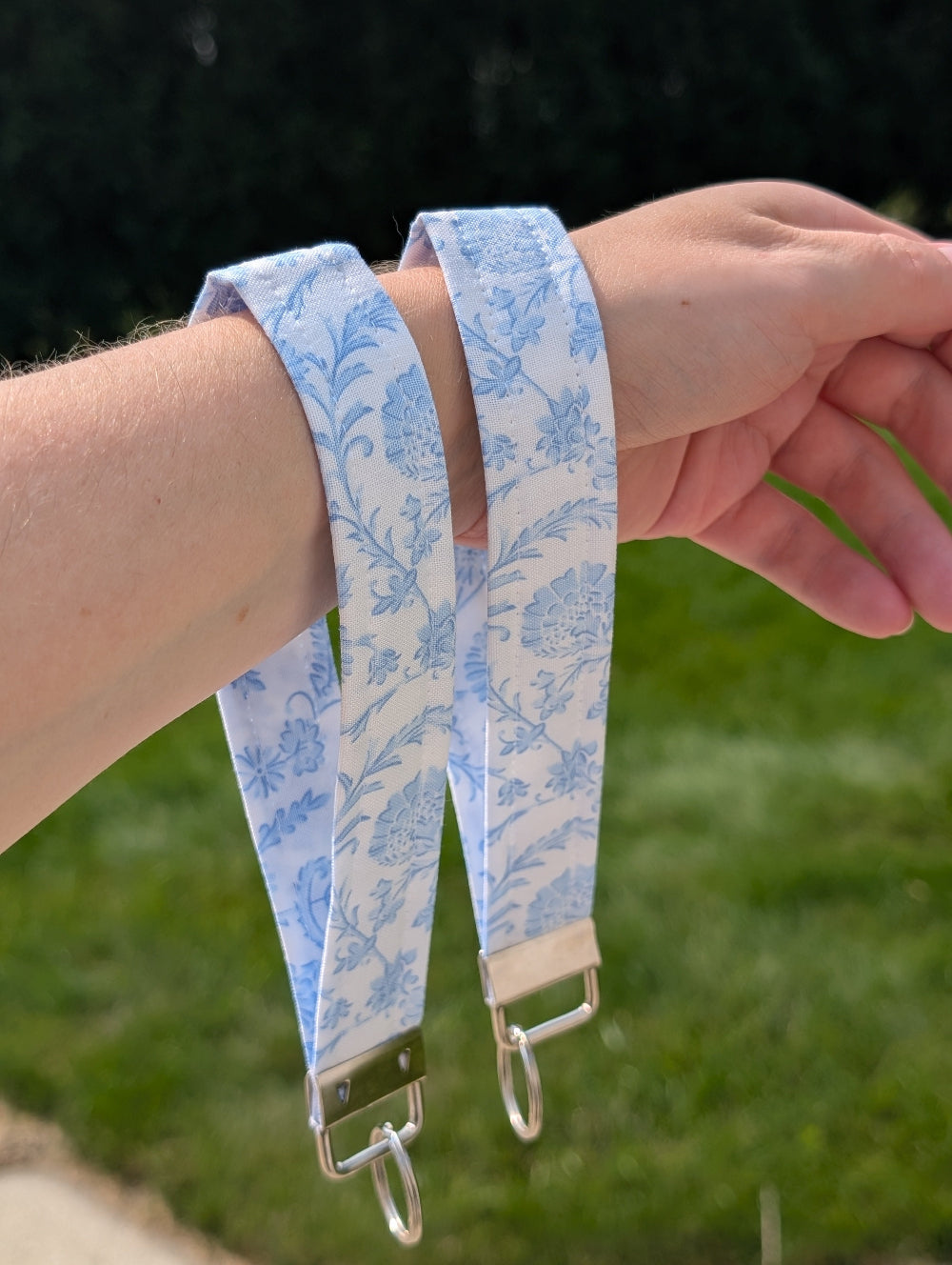 Blue floral strap with metal keychain on a person's wrist against a green outdoor background