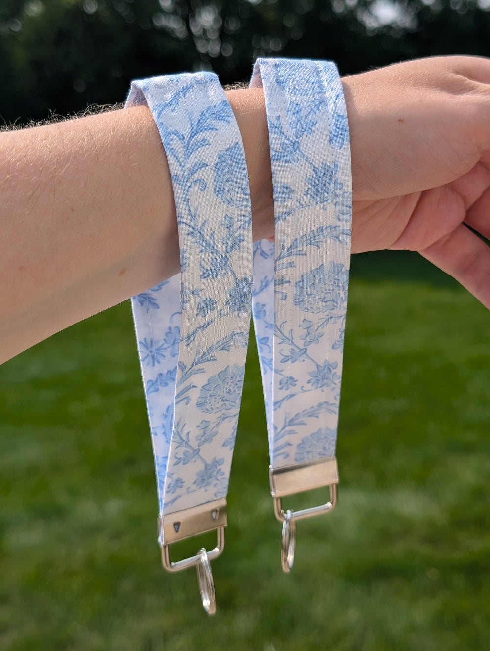 Floral patterned strap with a clasp held by a person against a green outdoor background