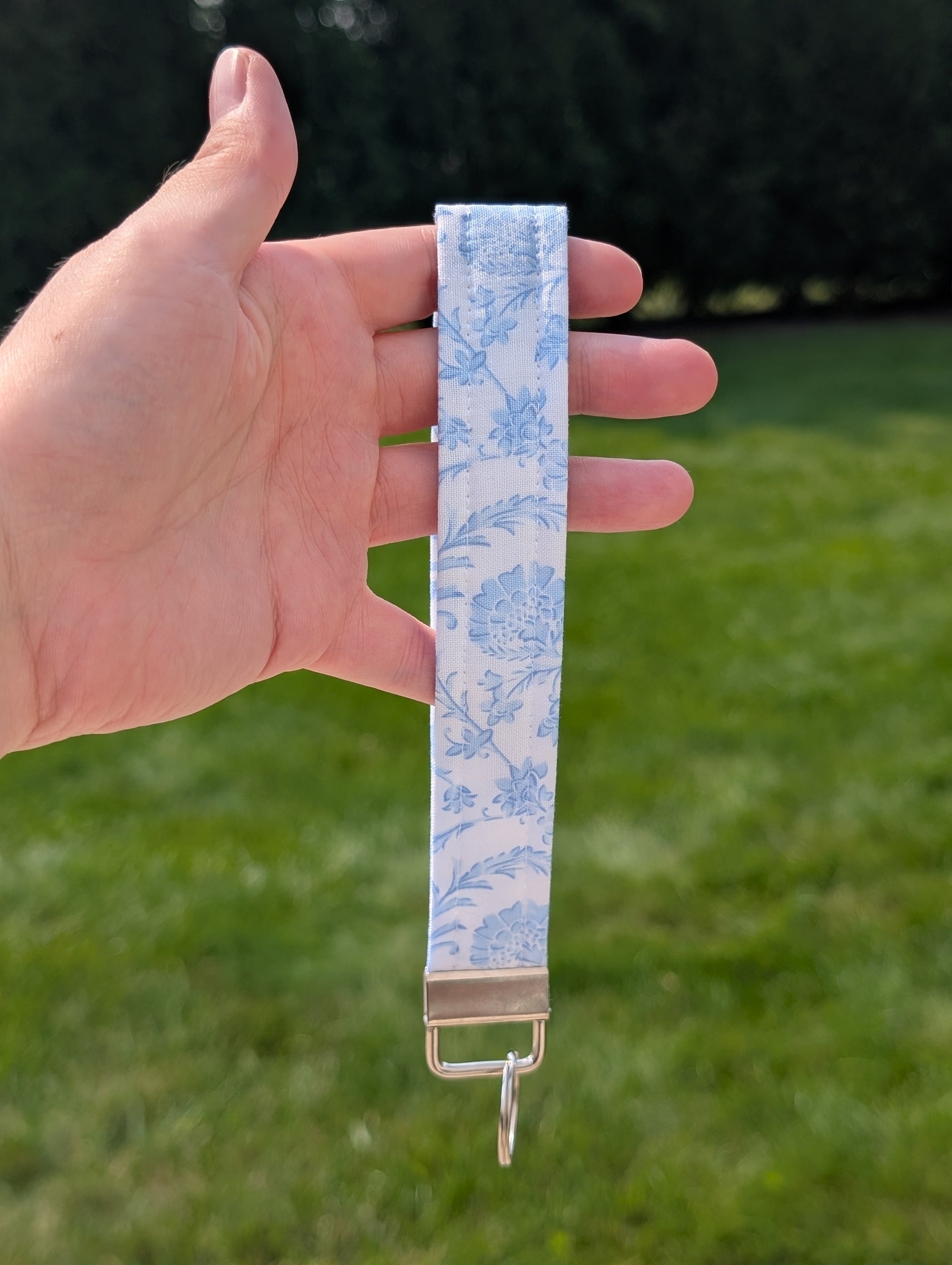 Hand holding a blue and white patterned strap with a metal buckle against a grassy background