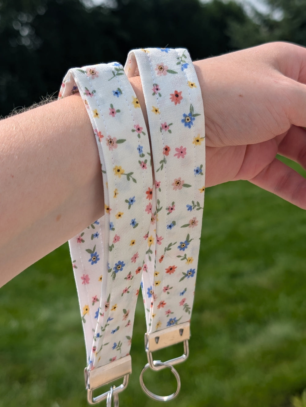 Floral patterned strap with a keyring held by a person against a blurred green background