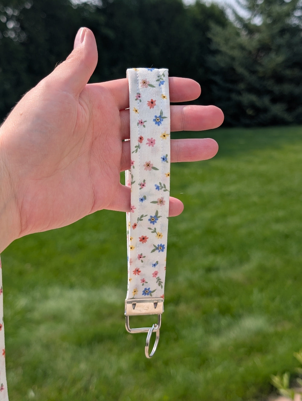 Floral-patterned strap held by a hand with a grassy background