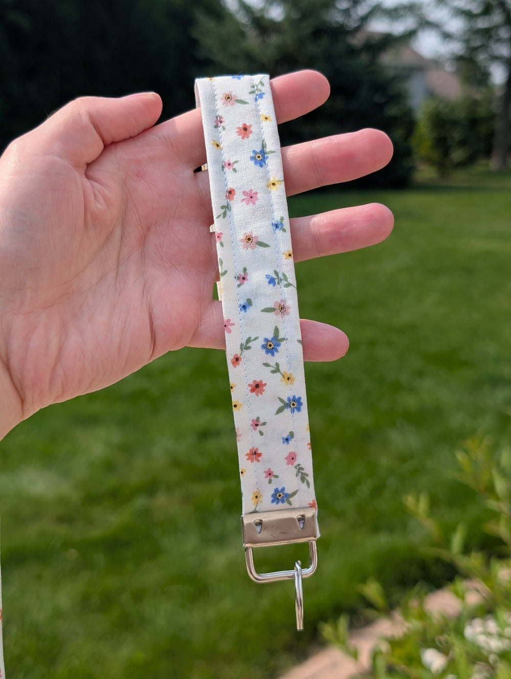 Floral-patterned keychain strap held by a hand with a green outdoor background