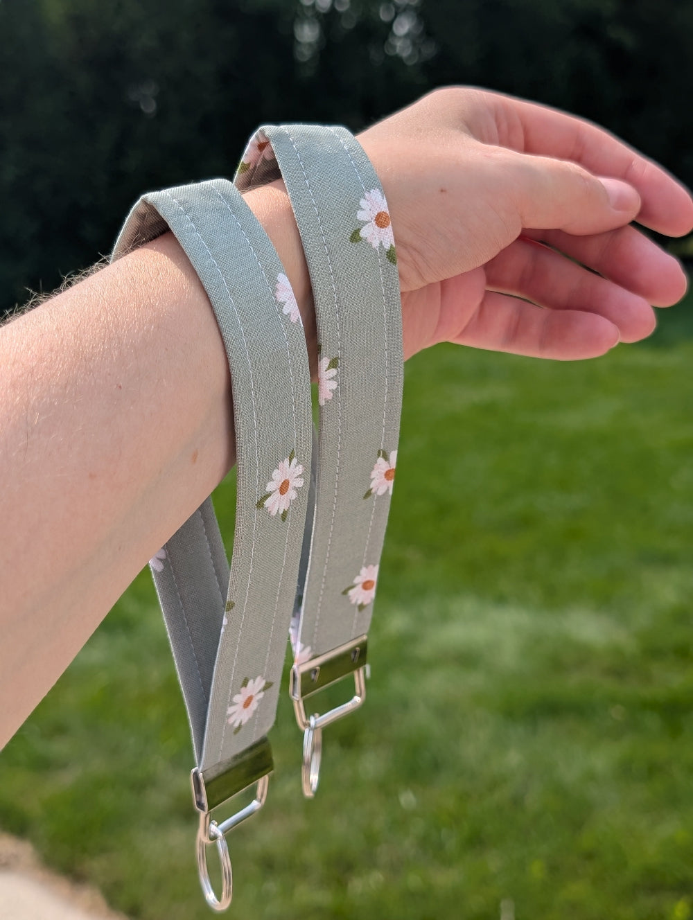 Green wristlet with floral pattern held by a hand against a blurred green background