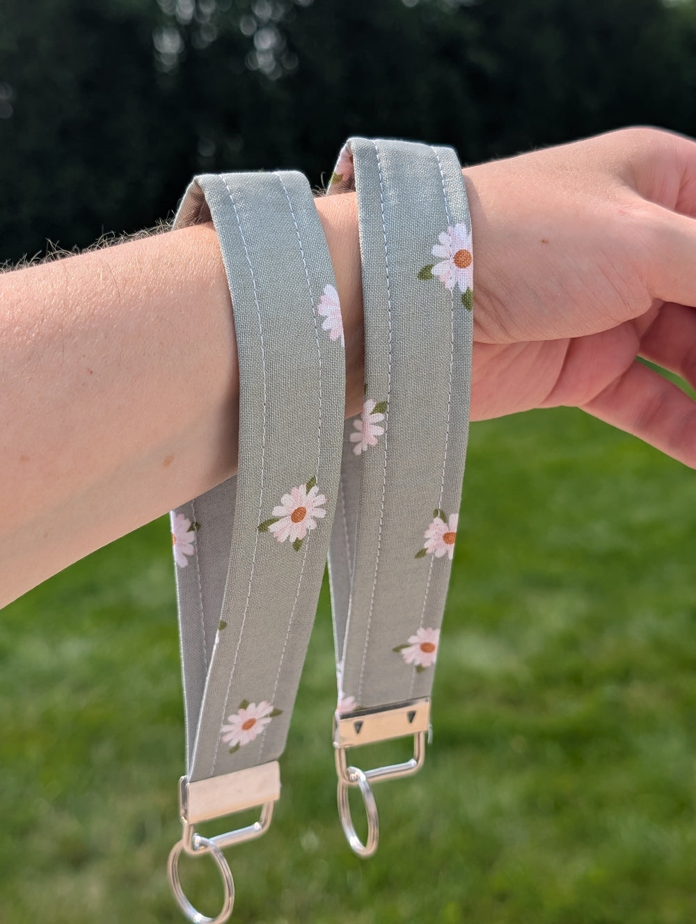Green wristlet strap with floral pattern held by a person against a blurred green background