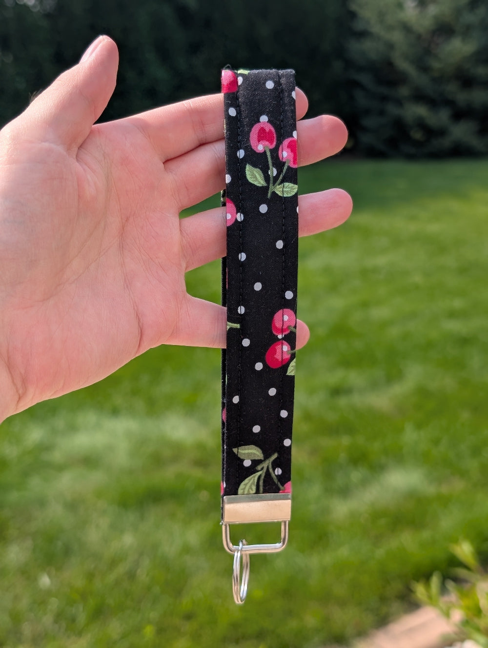 Hand holding a keychain with floral design against a grassy background