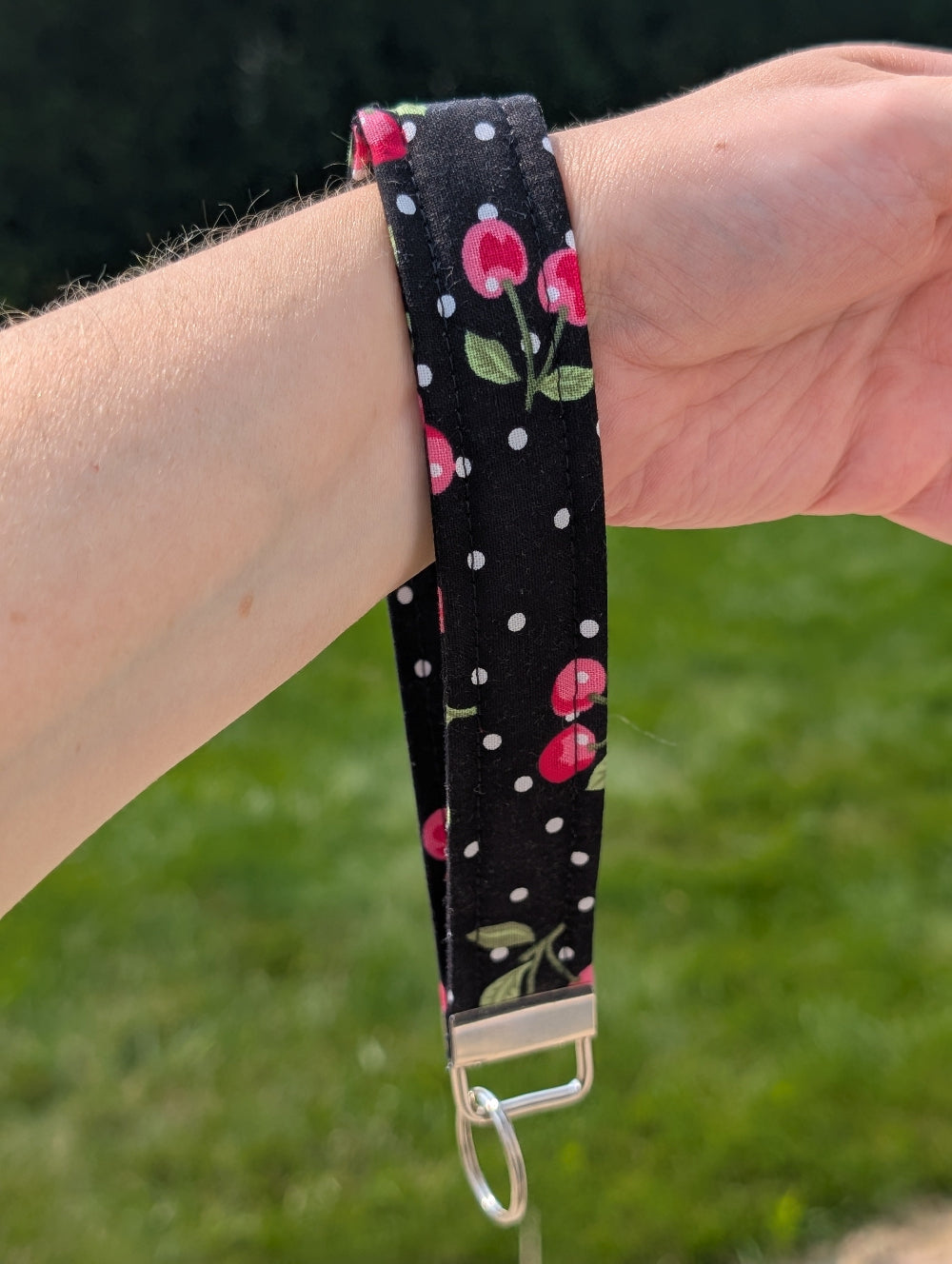Wristlet with cherry pattern on a person's wrist against a grassy background