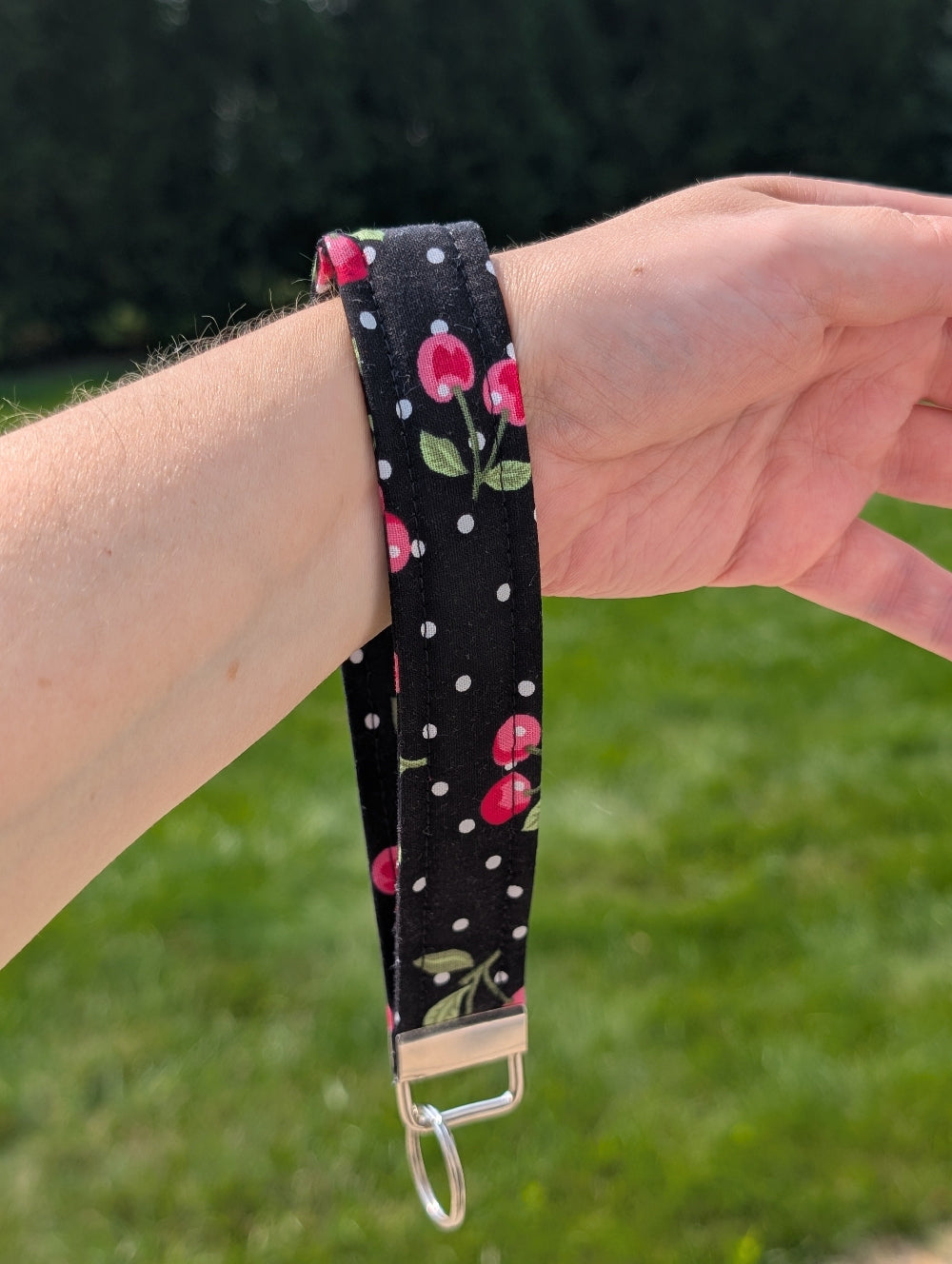Wristlet with cherry design and polka dots held by a person outdoors.