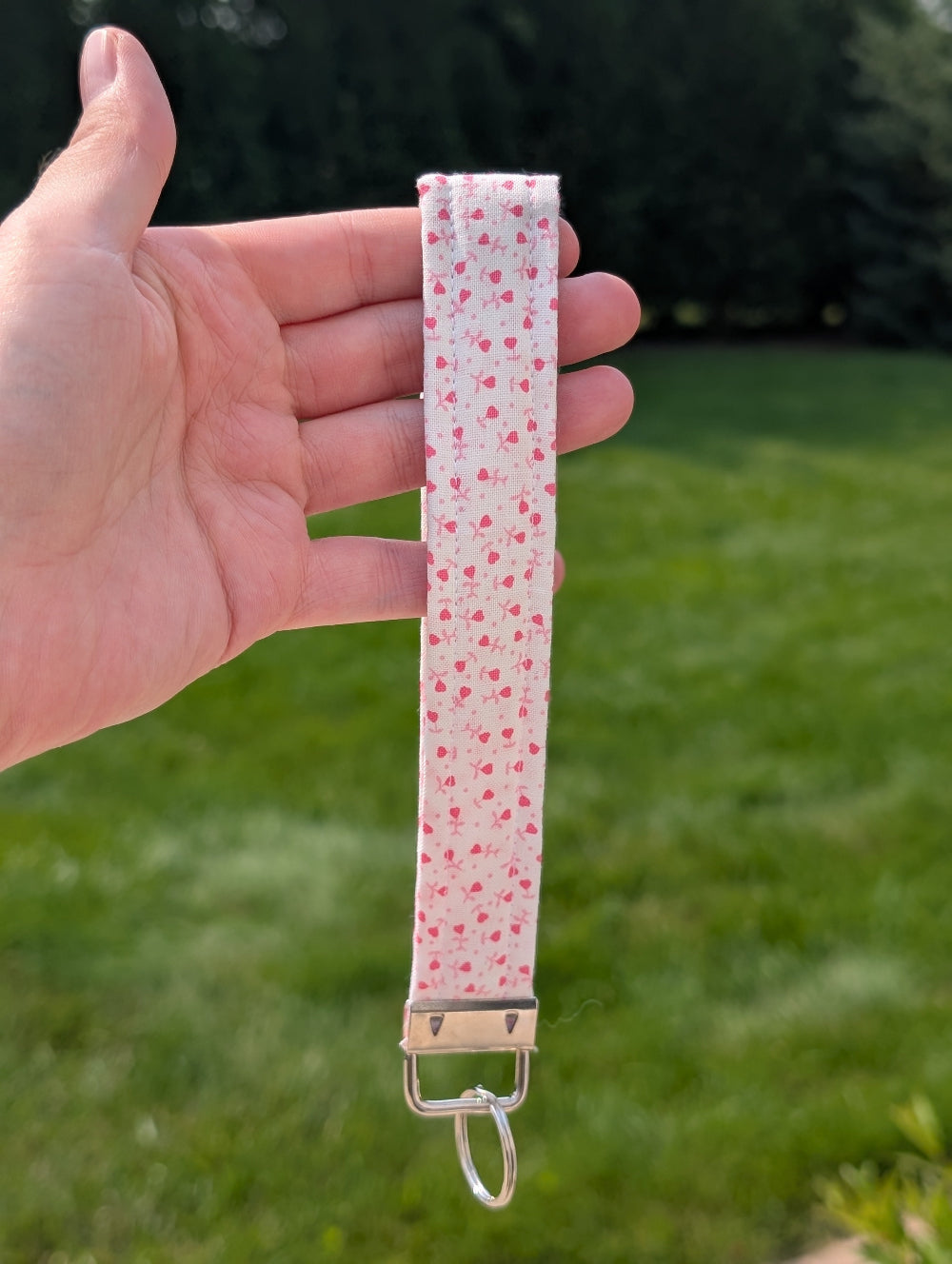 Hand holding a pink fabric keychain with a pattern against a grassy background