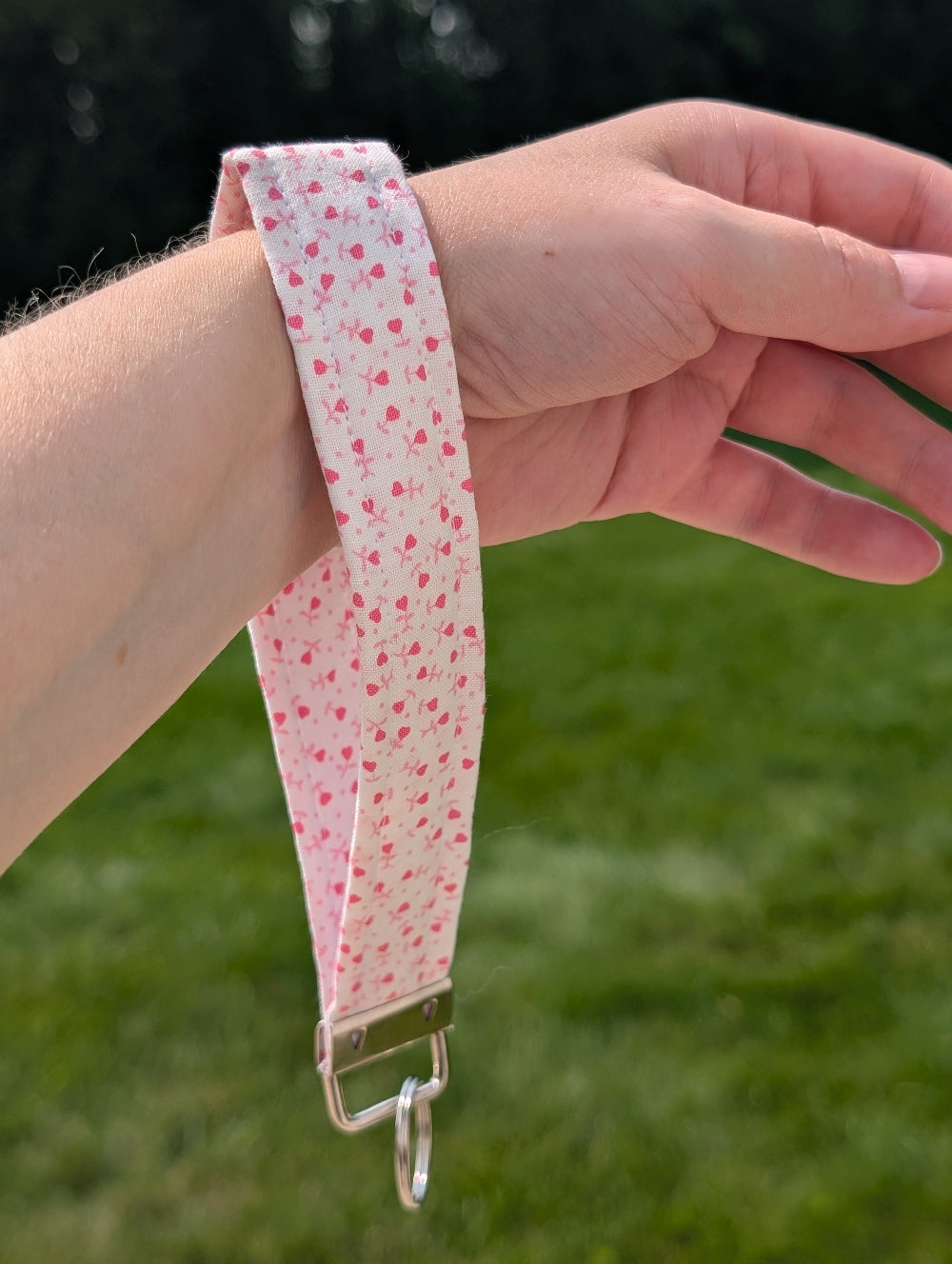 Hand wearing a pink fabric wristlet with a metal clasp against a grassy background